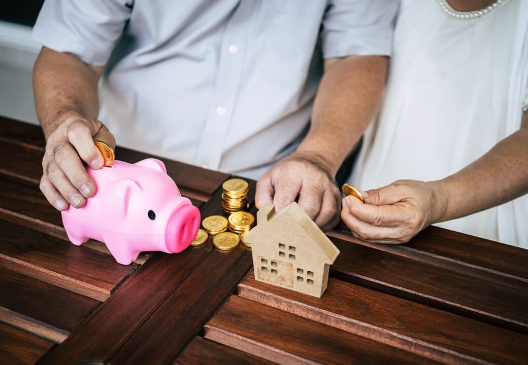 Duas pessoas com porquinhos, moedas e uma casinha, fazendo planos para o futuro financeiro