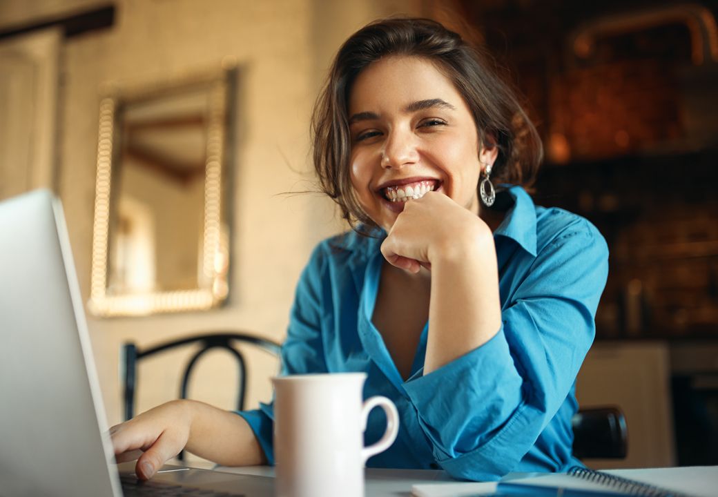 jovem mulher sorrindo em casa no computador ao antecipar o saque aniversário do seu FGTS