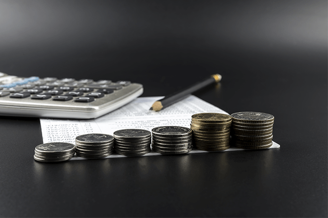 calculadora, papel e lápis e moedas usadas em um cálculo de imposto de renda