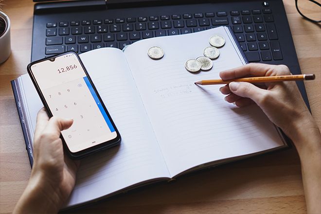 foto da mão fazendo contas em um caderno, na calculadora, contando dinheiro